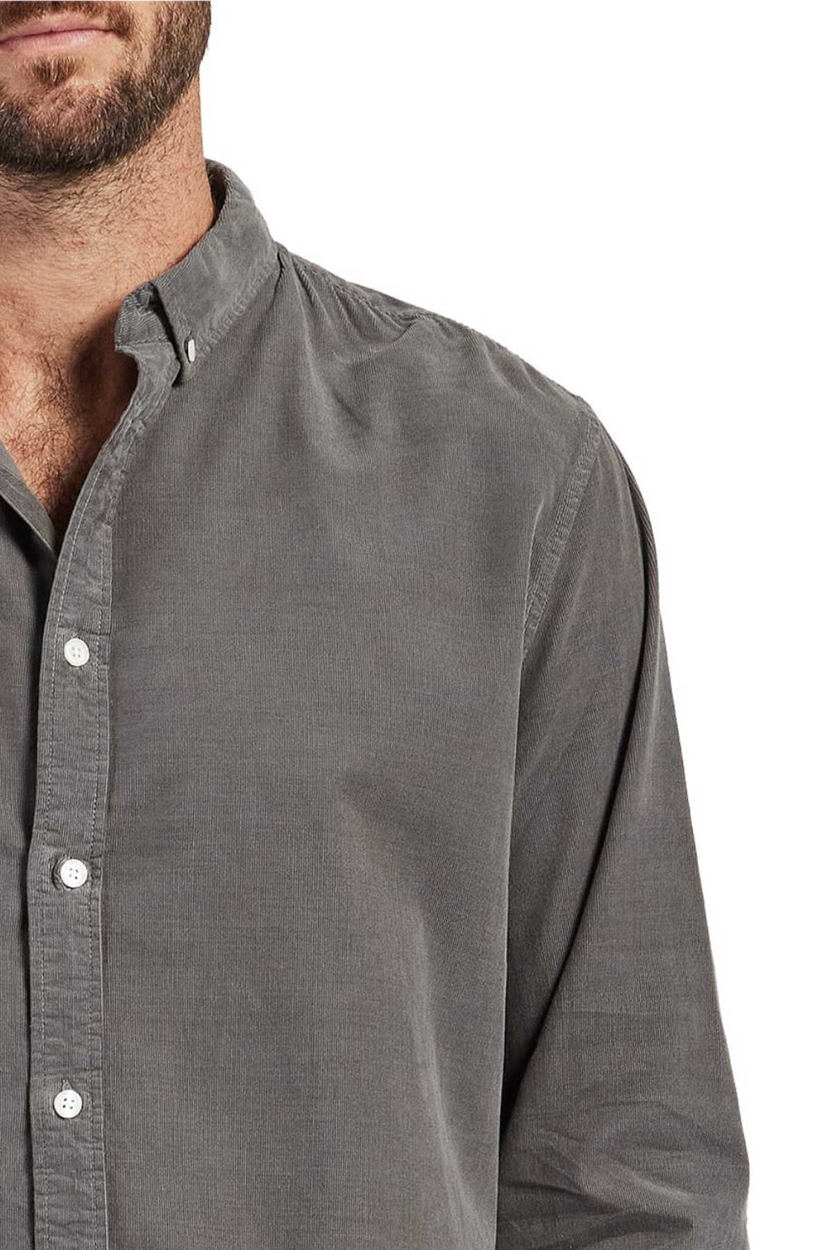 A close-up of a person wearing a grey Academy Brand Micro Cord Shirt with a collar. The person's face is partially cropped out, showing only a bit of their chin and beard. The shirt, made from 100% cotton, features white buttons and button-down points, creating a polished look.