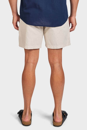 A person stands facing away, wearing a navy blue shirt, Academy Brand Oahu Short in vintage cotton twill, and black slide sandals with cork soles, set against a plain white background.