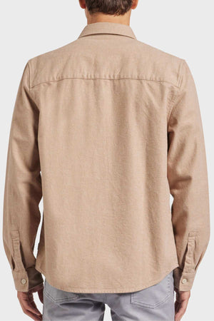 A person with short hair seen from the back, wearing an Academy Brand Oakland Overshirt in light brown. This stylish longsleeve overshirt is crafted from premium yarn dye twill and made of 100% cotton; it features buttoned cuffs, a collar, and a seam running horizontally across the shoulder blades. The individual is also sporting light gray pants.