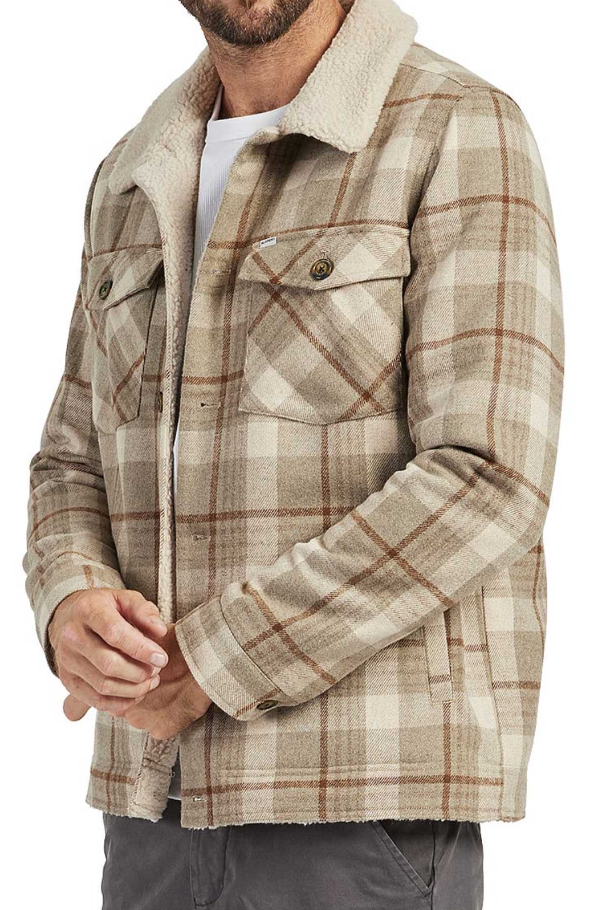 Man wearing the Academy Brand Quincy Jacket in beige and brown plaid, crafted from a wool blend with a white faux shearling collar, styled with a white undershirt and gray pants. The jacket has buttoned chest pockets; man's face is partially out of frame.