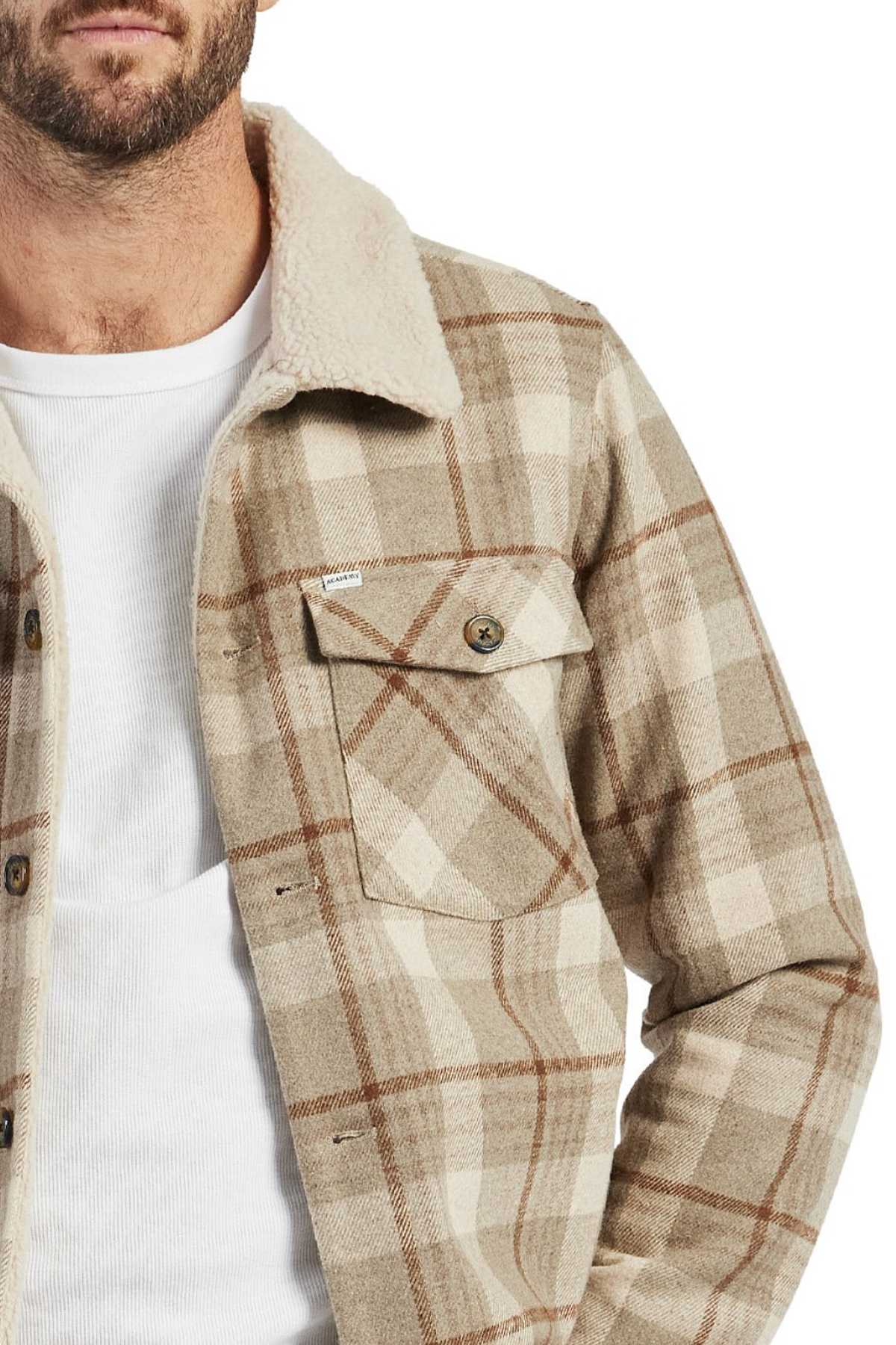 A man is shown from shoulders to waist wearing a white shirt and the Academy Brand Quincy Jacket, a beige plaid wool blend sherpa-lined jacket with a buttoned chest pocket. Only his lower face is visible.