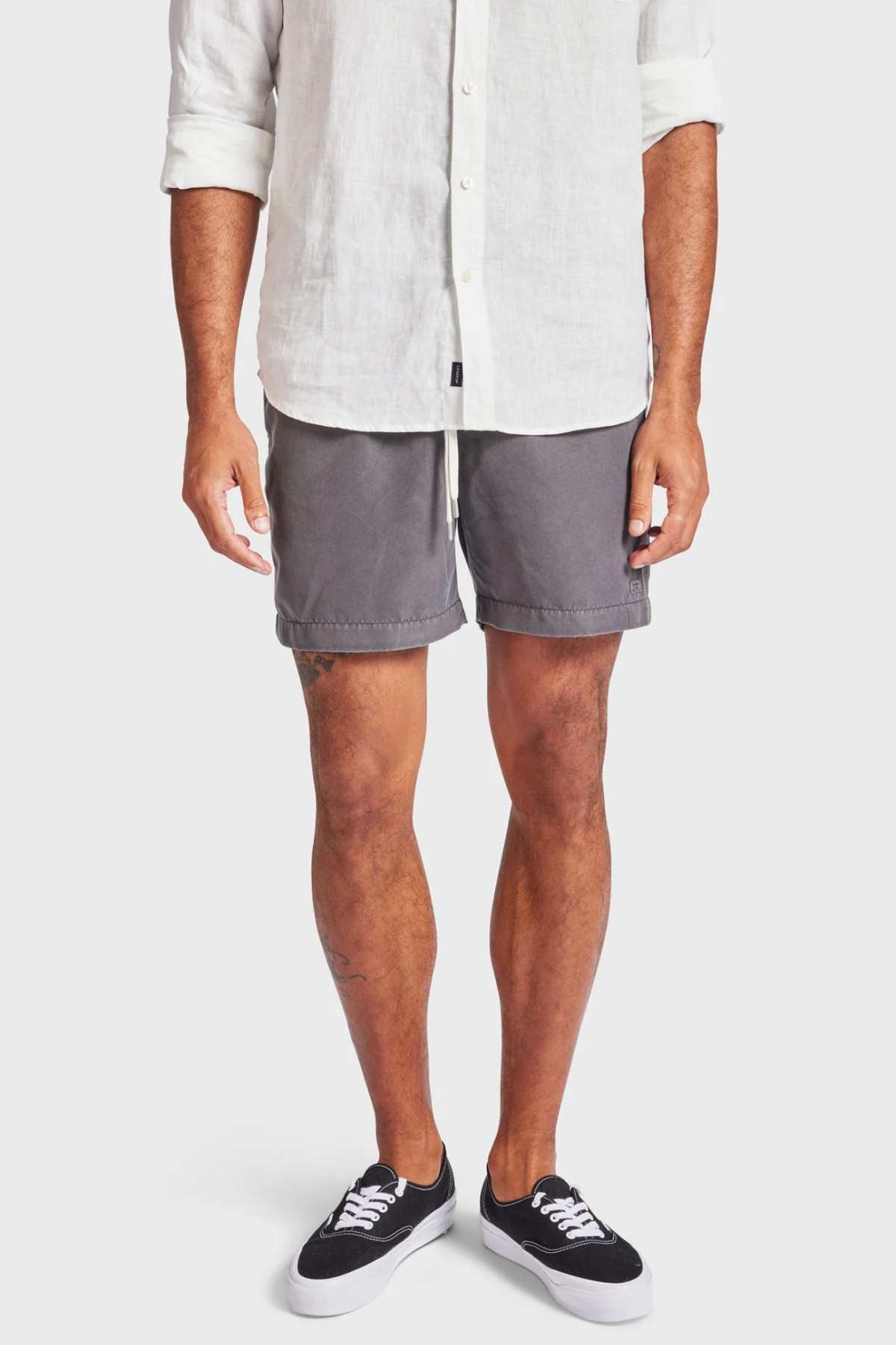 A person is wearing a tailored fit white button-up shirt, Academy Brand Teamster Boardy quick-dry gray swim shorts, and black sneakers with white soles. They stand against a plain white background, hands resting by their sides.