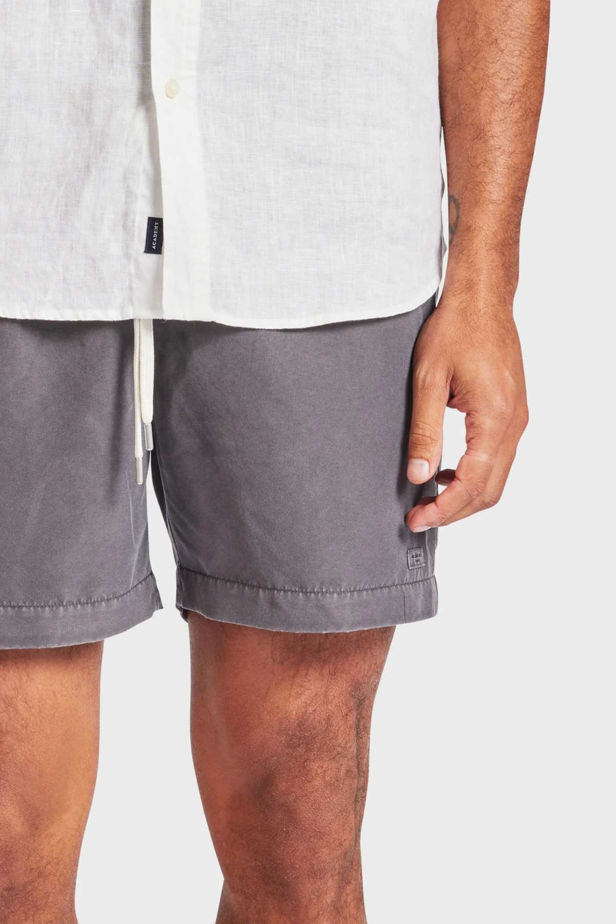 A person wearing a white button-up shirt and Academy Brand Teamster Boardy gray shorts stands against a plain background, showing only the lower torso and arms.