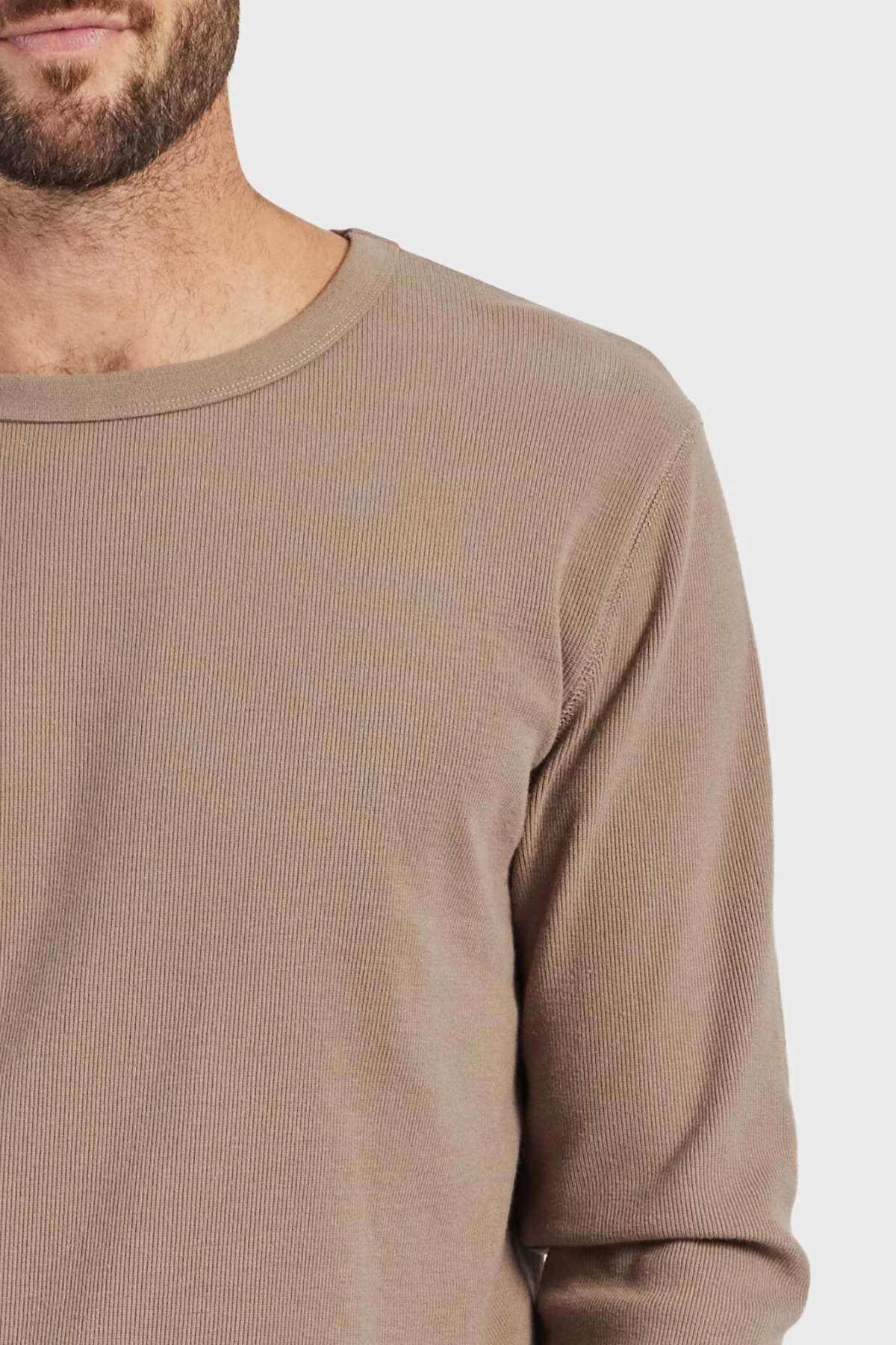 A close-up of a person wearing the Academy Brand Workers Crew, highlighting its beige color and French rib construction against a plain background. Only the upper torso and part of the bearded face are visible.