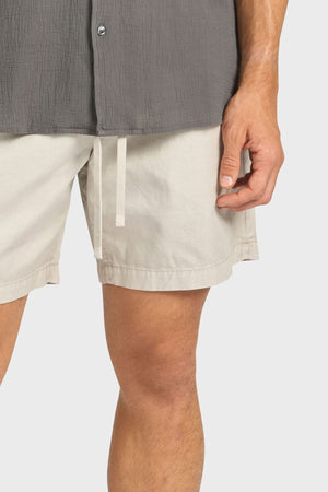 A person wears a gray textured shirt and Academy Brand Oahu Short in light beige with a relaxed volley silhouette, shown from mid-torso to mid-thigh against a plain background.