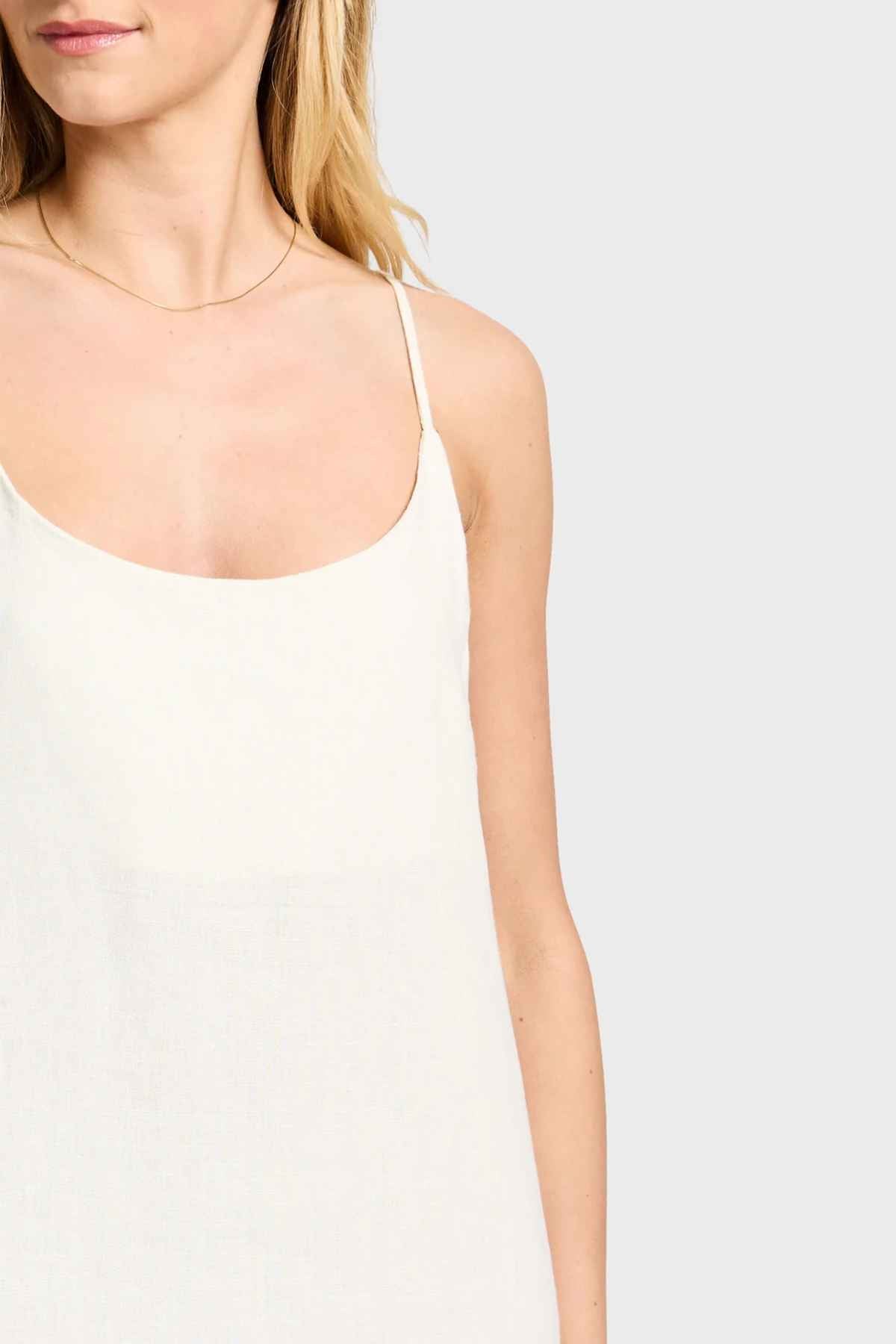 A woman with blonde hair is wearing the stylish Academy Women Essential Linen Slip Dress, featuring adjustable straps, and is accessorized with a delicate thin gold necklace against a plain background.