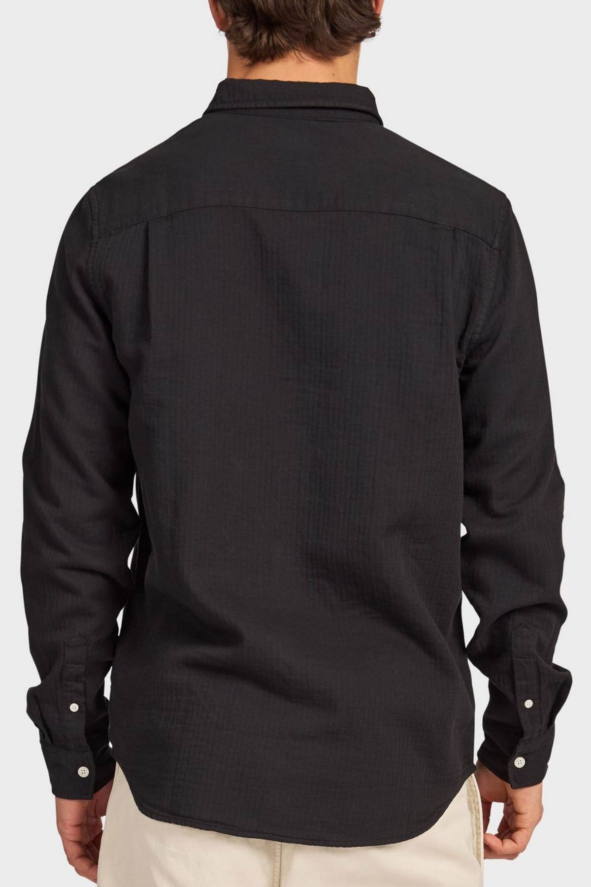 A person is shown from behind wearing an Academy Brand Harry Double Cloth Shirt in black with light pants, standing against a plain light gray background.