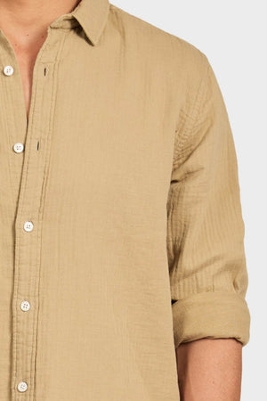 A person wearing a light brown Academy Brand Harry Double Cloth Shirt, a men's casual cotton shirt with a textured finish, left sleeve rolled up and partially unbuttoned, shown from shoulders to waist on a plain background.