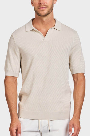 A man wearing the Academy Brand Jonny Textured Knit Polo in light beige, featuring a relaxed collar and no buttons, paired with light drawstring pants, stands against a plain background.
