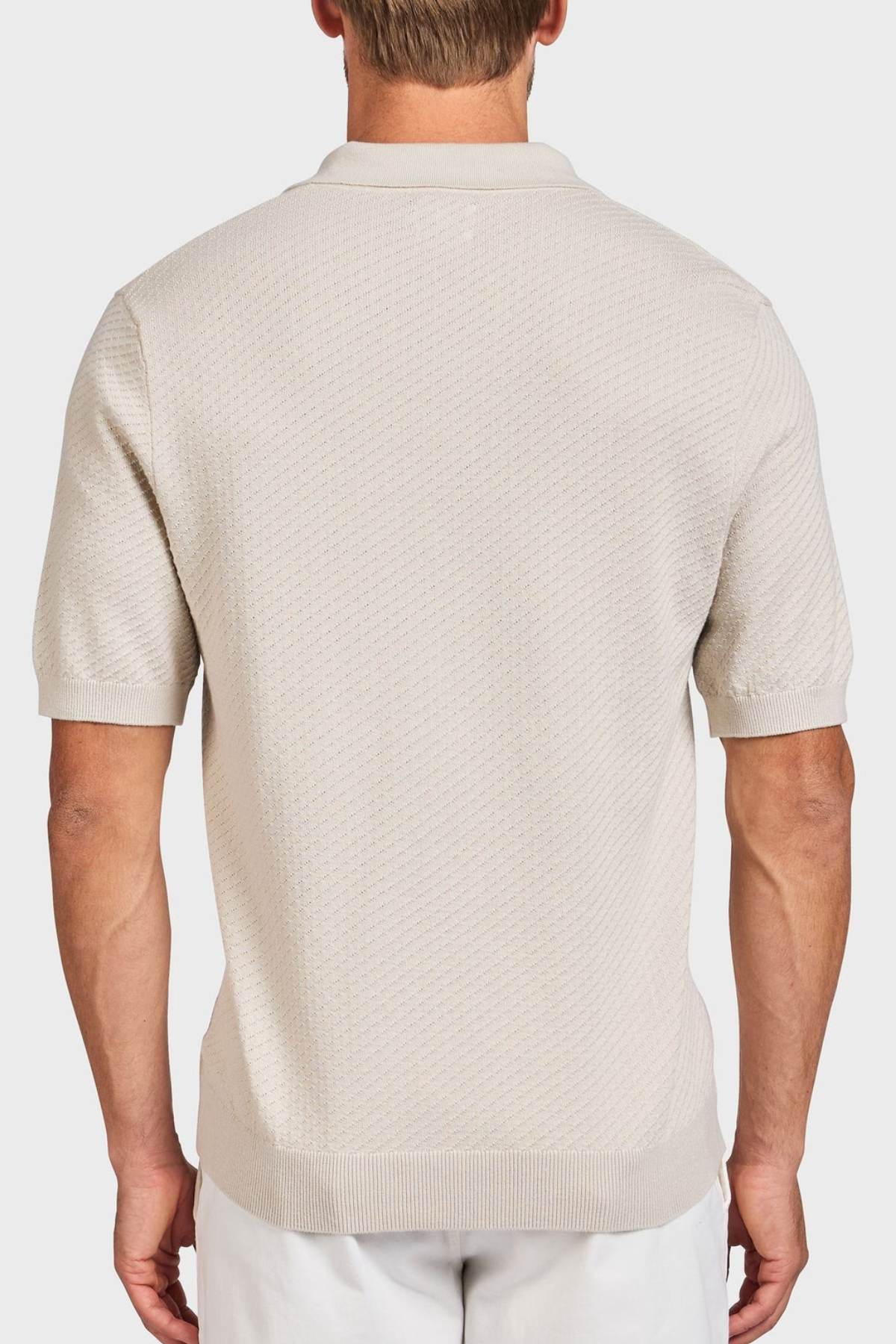 A man is seen from behind wearing the Academy Brand Jonny Textured Knit Polo in light beige, featuring a subtle textured pattern with ribbed hem and sleeve cuffs, paired with white pants.