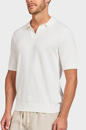 A man stands against a plain white background wearing the Academy Brand Jonny Textured Knit Polo in cotton with a collar and V-neck, paired with light beige pants.
