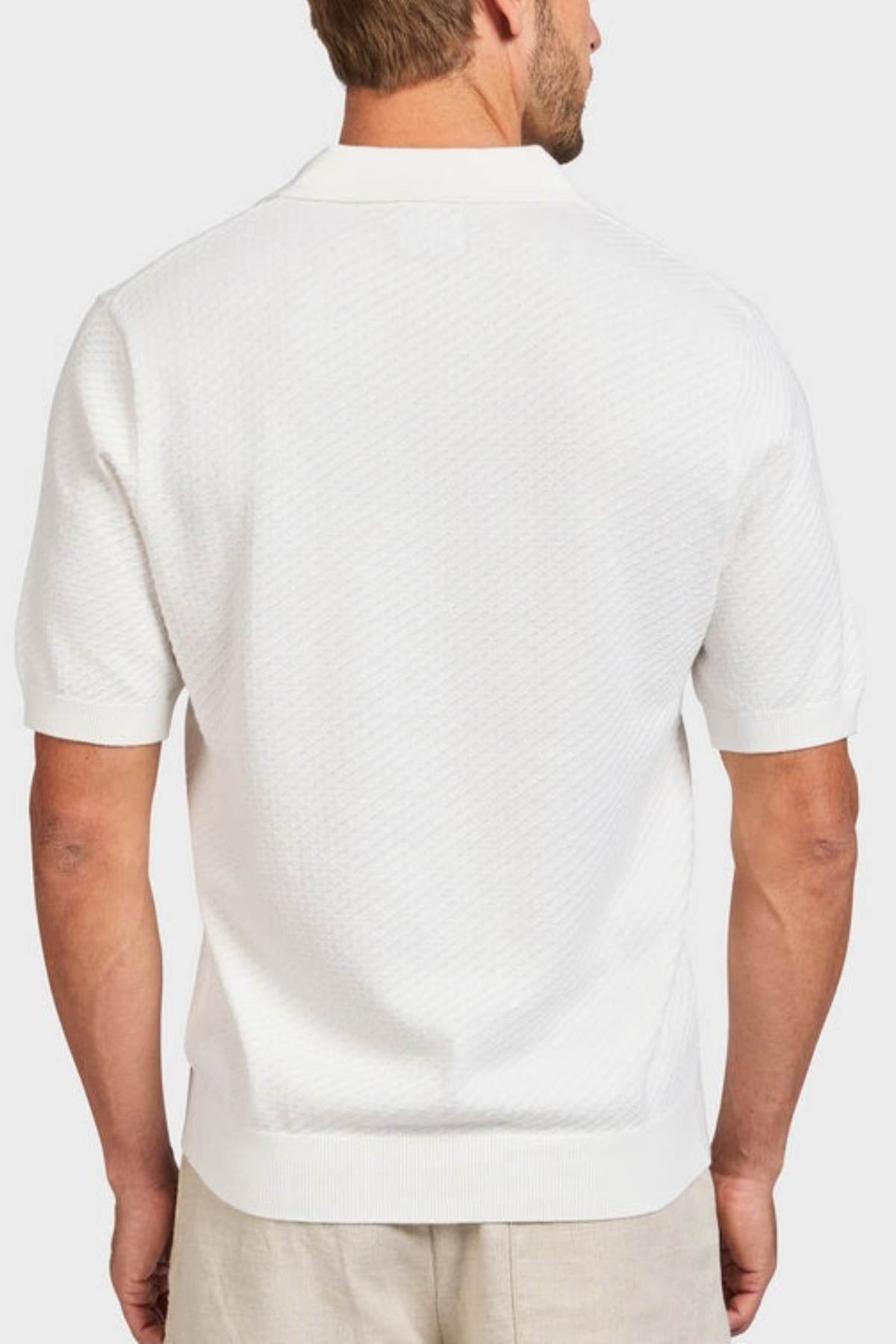 A man is shown from behind wearing the Academy Brand Jonny Textured Knit Polo in soft textured cotton with a subtle pattern, ribbed cuffs and waistband, paired with light pants against a plain white background.