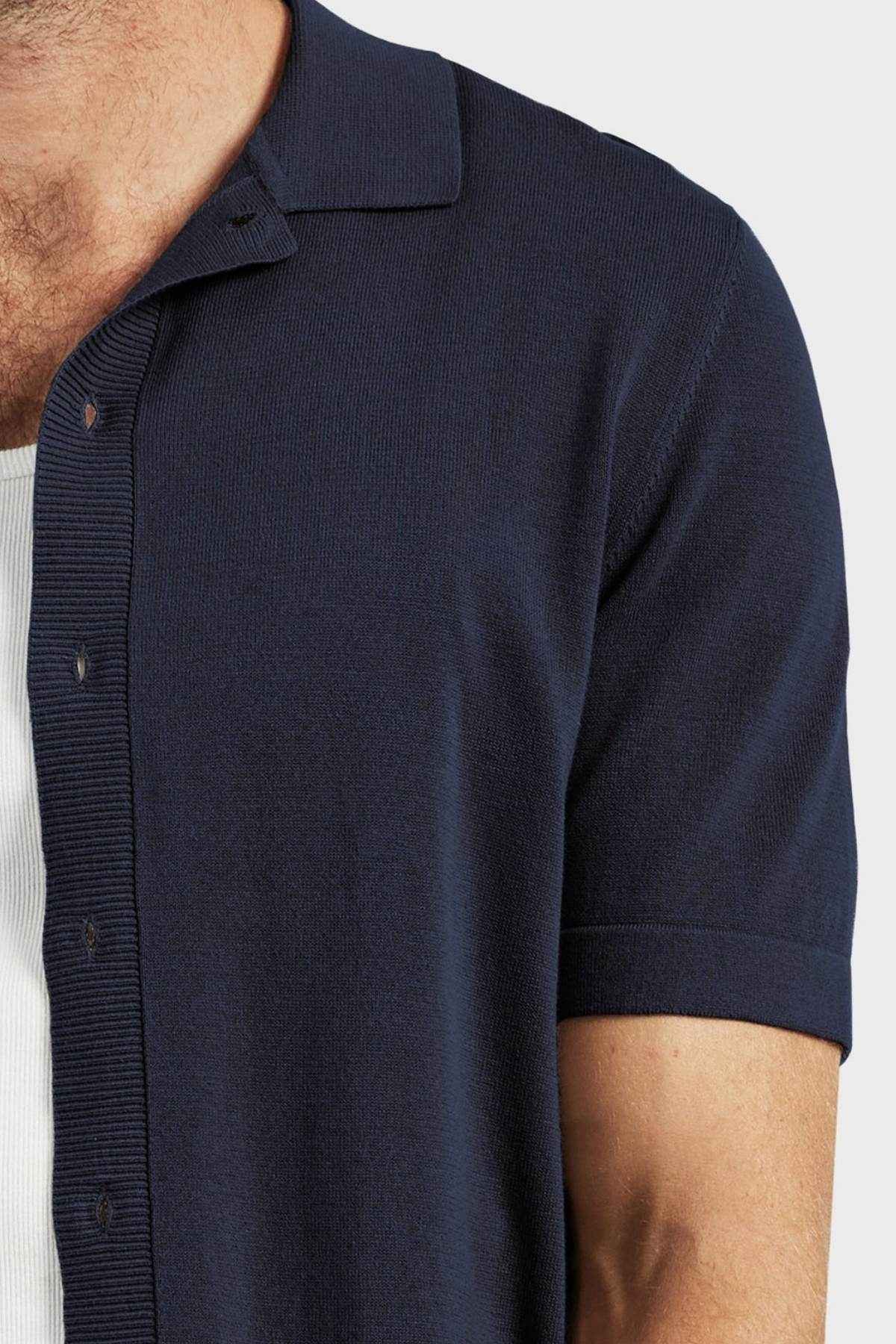 A close-up shows a person wearing the Academy Brand Jackson Knit Short Sleeve Shirt in navy blue over a white ribbed undershirt, with only their upper torso and part of one arm visible.