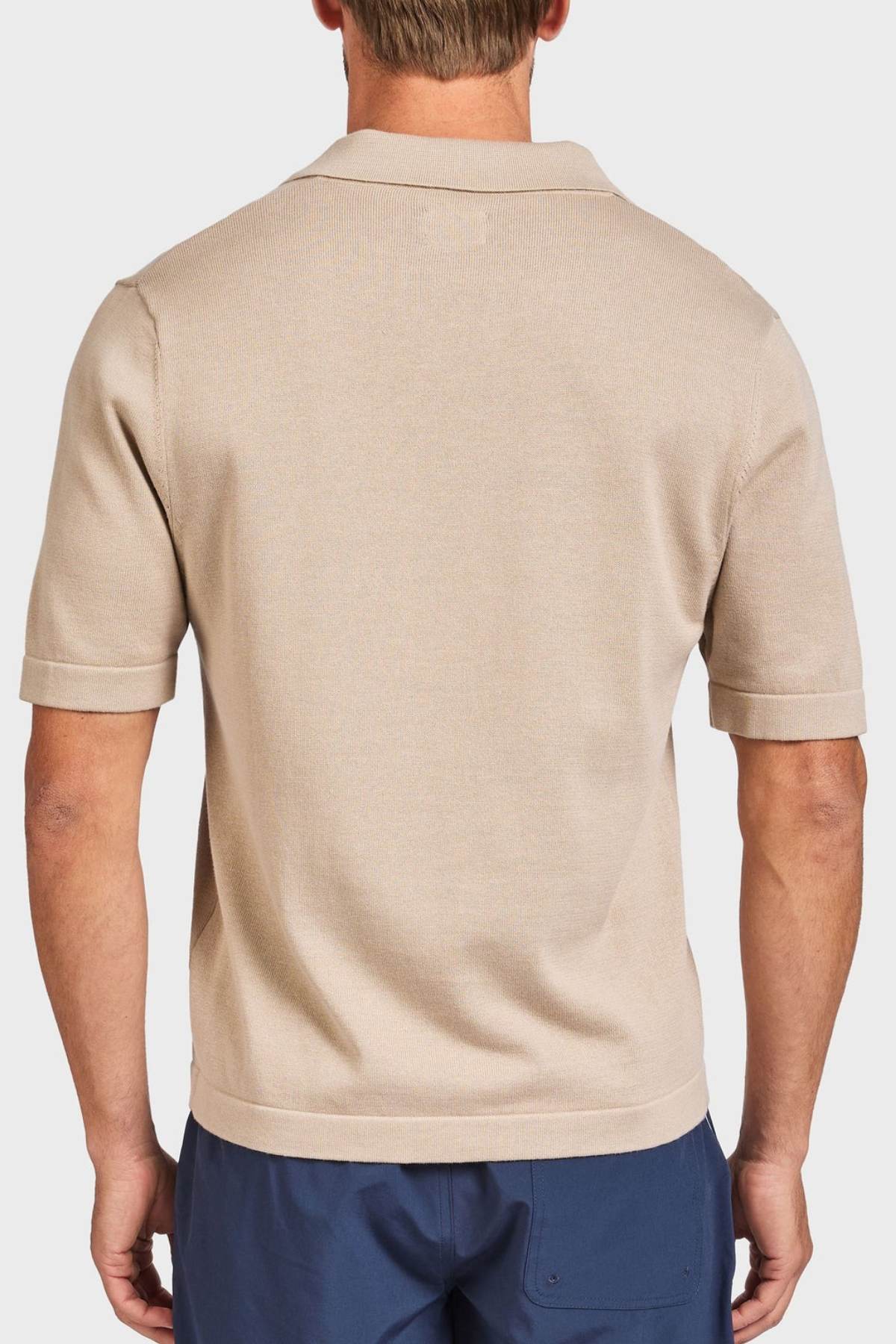 A man seen from behind wears the Academy Brand Jackson Knit Short Sleeve Shirt in beige and navy blue pants, standing against a plain white background.