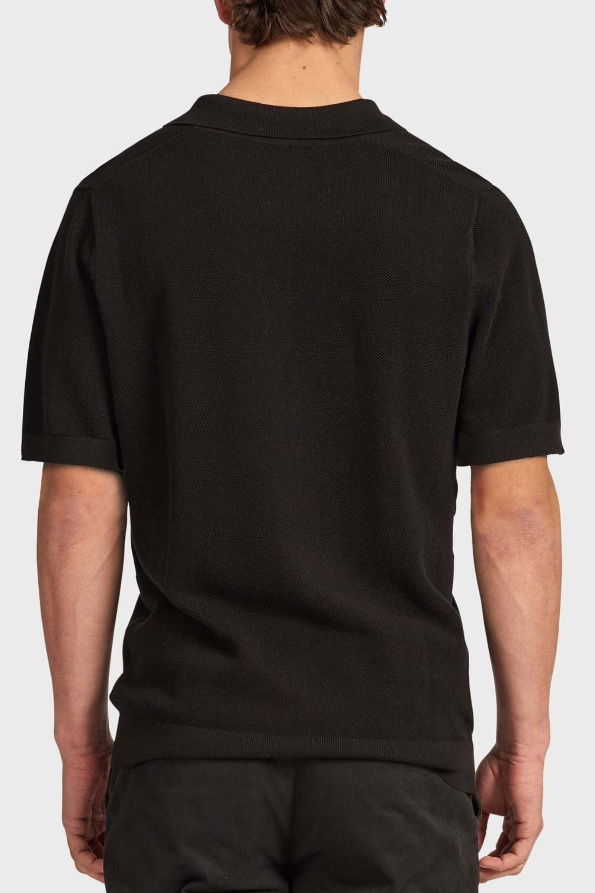 Someone is seen from behind wearing the Academy Brand Riley Knit Polo in black, made from breathable fabric, against a plain light background.