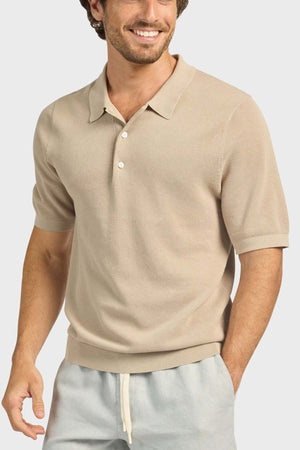 A man in the Academy Brand Riley Knit Polo—beige, breathable—and light gray drawstring pants smiles with one hand in his pocket against a plain, light background.