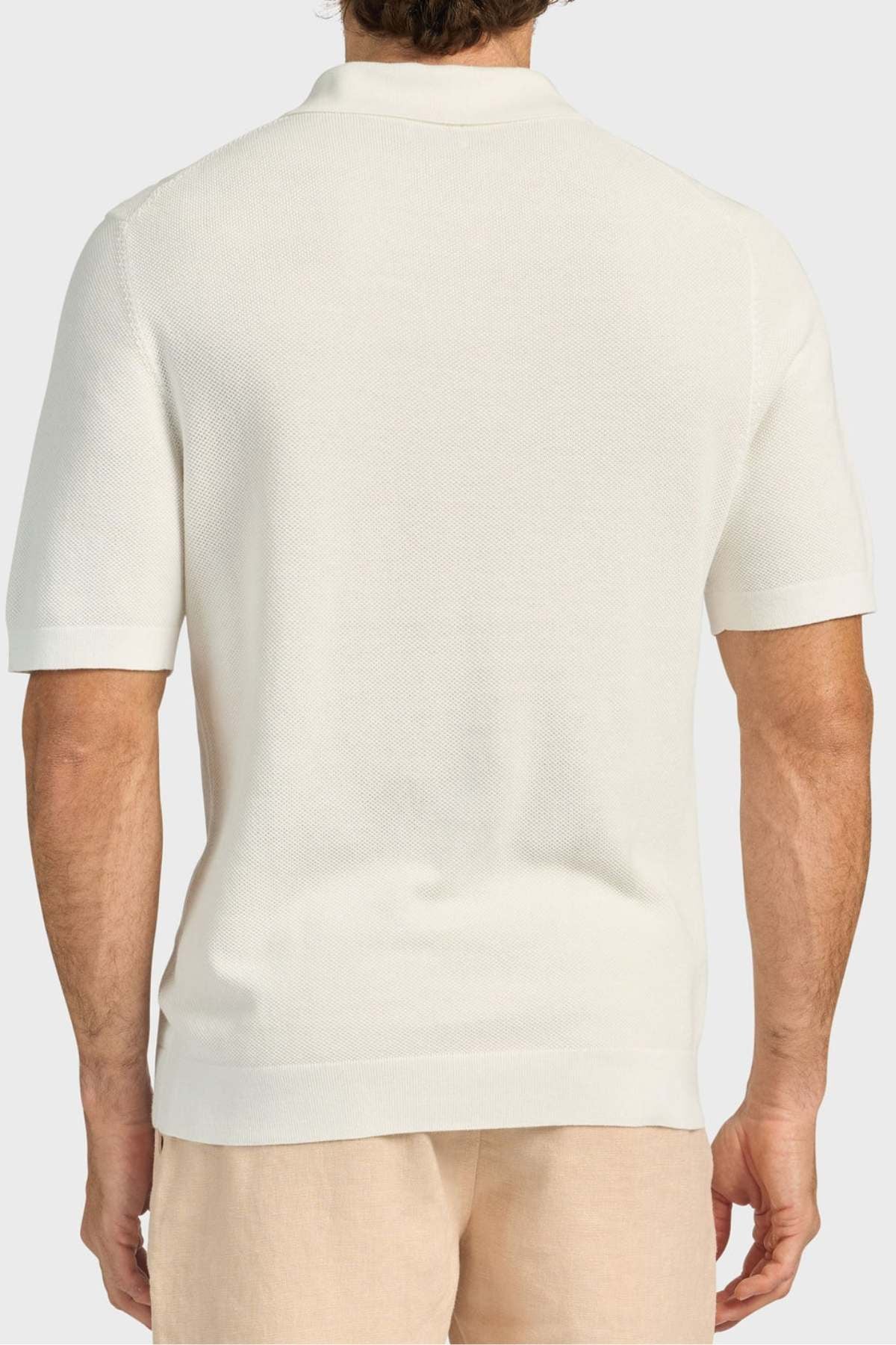 A man is seen from behind wearing an Academy Brand Riley Knit Polo in off-white and beige shorts. The polo’s breathable fabric ensures comfort. He stands before a plain, light-colored background.