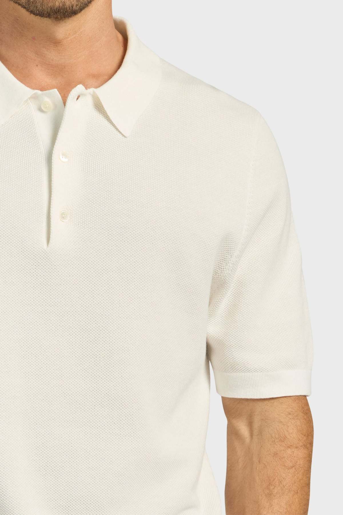 A man wearing the Academy Brand Riley Knit Polo—a short-sleeve, off-white textured polo made from breathable fabric—is shown from shoulders to waist against a plain light background.