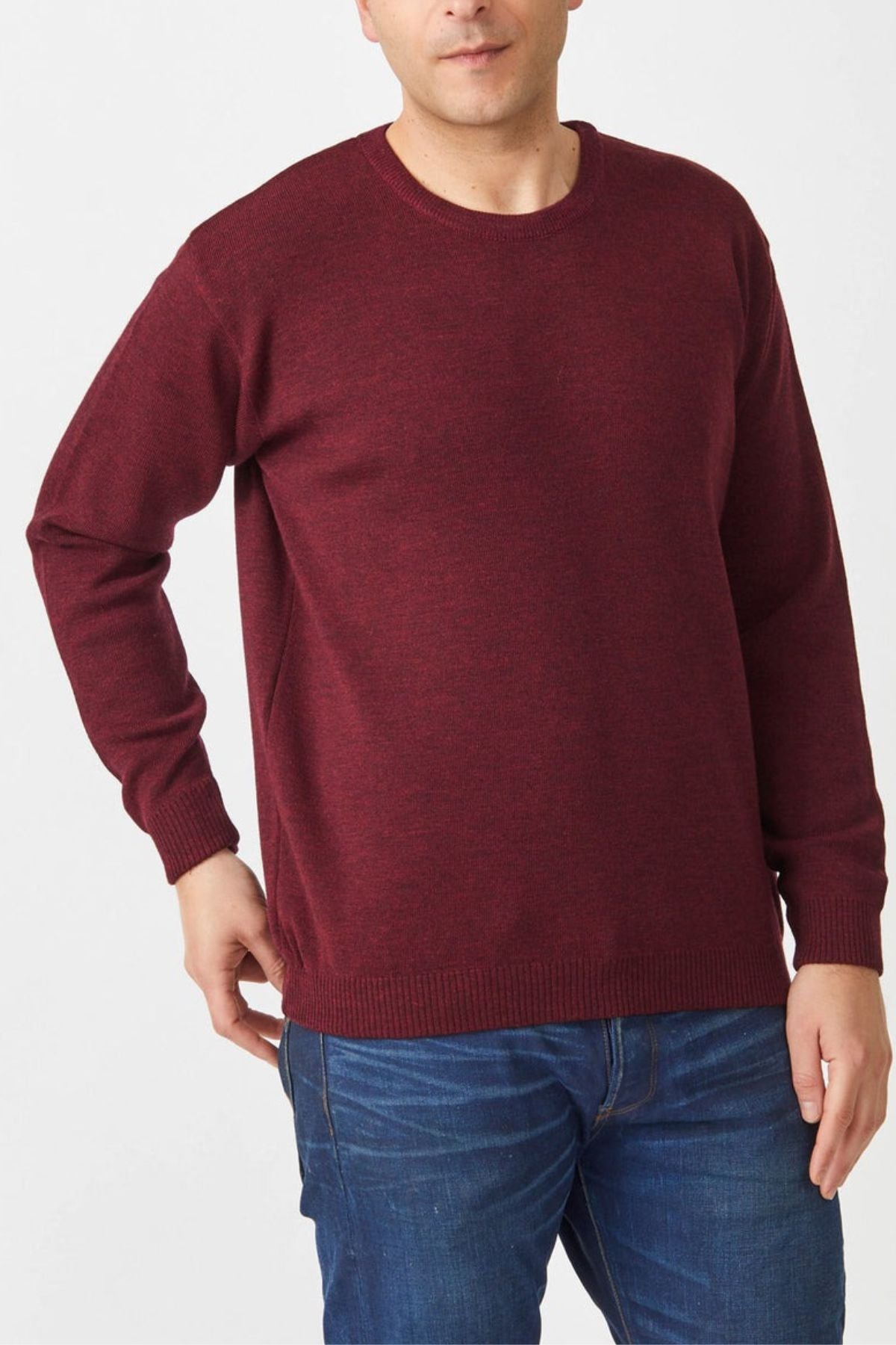 Wearing an Aklanda Crew Pullover in maroon over classic denim blue jeans, a person stands against a plain white background. With one hand on their hip, they highlight the comfort of this Australian-made merino wool jumper featuring a round neckline.