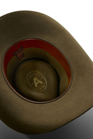 A close-up of the inside of an olive-green Akubra Snowy River hat, showing a brown leather band, a size tag marked "57," and a logo with the letter "A" plus "MAYSER 1800-1976" printed on the inner lining.