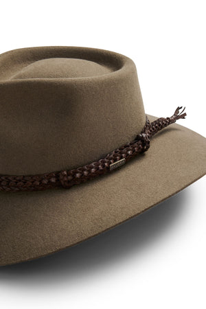 The Akubra The Brumby is a khaki felt hat with a wide brim, adorned with a braided brown leather band and metallic "Akubra" tag—ideal for bush festivals or Australian outback adventures. Shown on a white background.