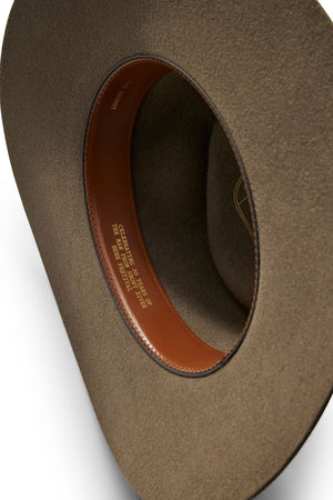 Close-up of the inside of an Akubra The Brumby hat, featuring a brown felt design and leather sweatband with gold embossed text. The hat rests on a white surface, capturing the essence of the Australian outback.