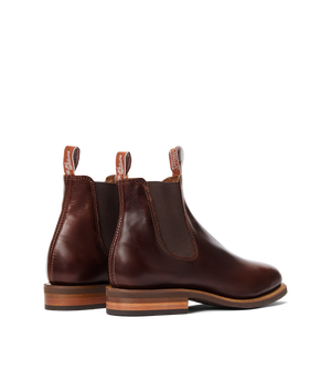 The RM Williams Moriarty Rubber Sole Boot is a brown Chelsea boot with a pull-up leather upper, elastic side panels, pull tabs, and stacked wooden heels, shown on a white background.