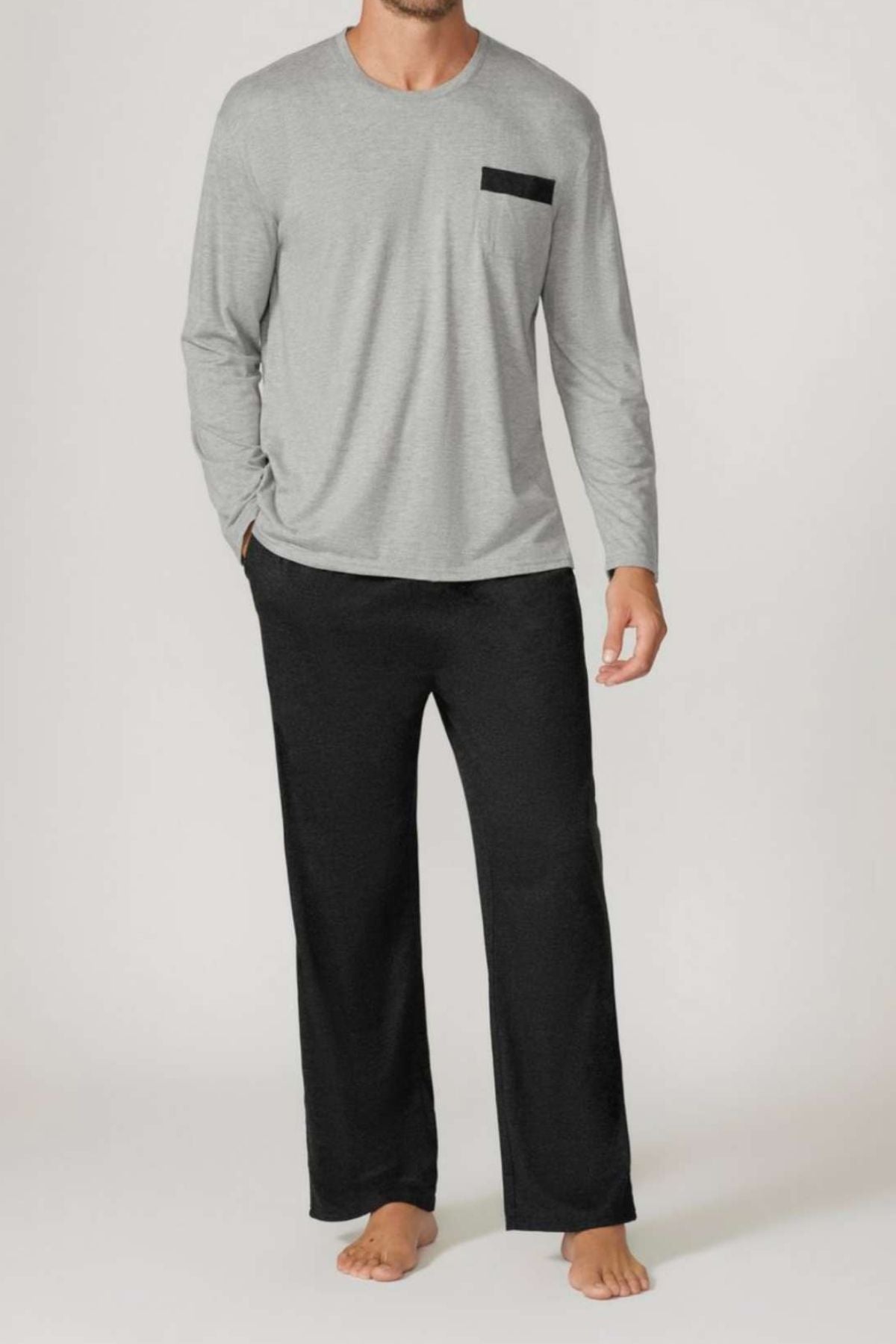 A man stands barefoot against a plain background wearing the Contare Country Bamboo Cotton Long Sleeve Set in light gray with a black chest pocket and loose black pajama pants, highlighting its stylish, breathable loungewear design.