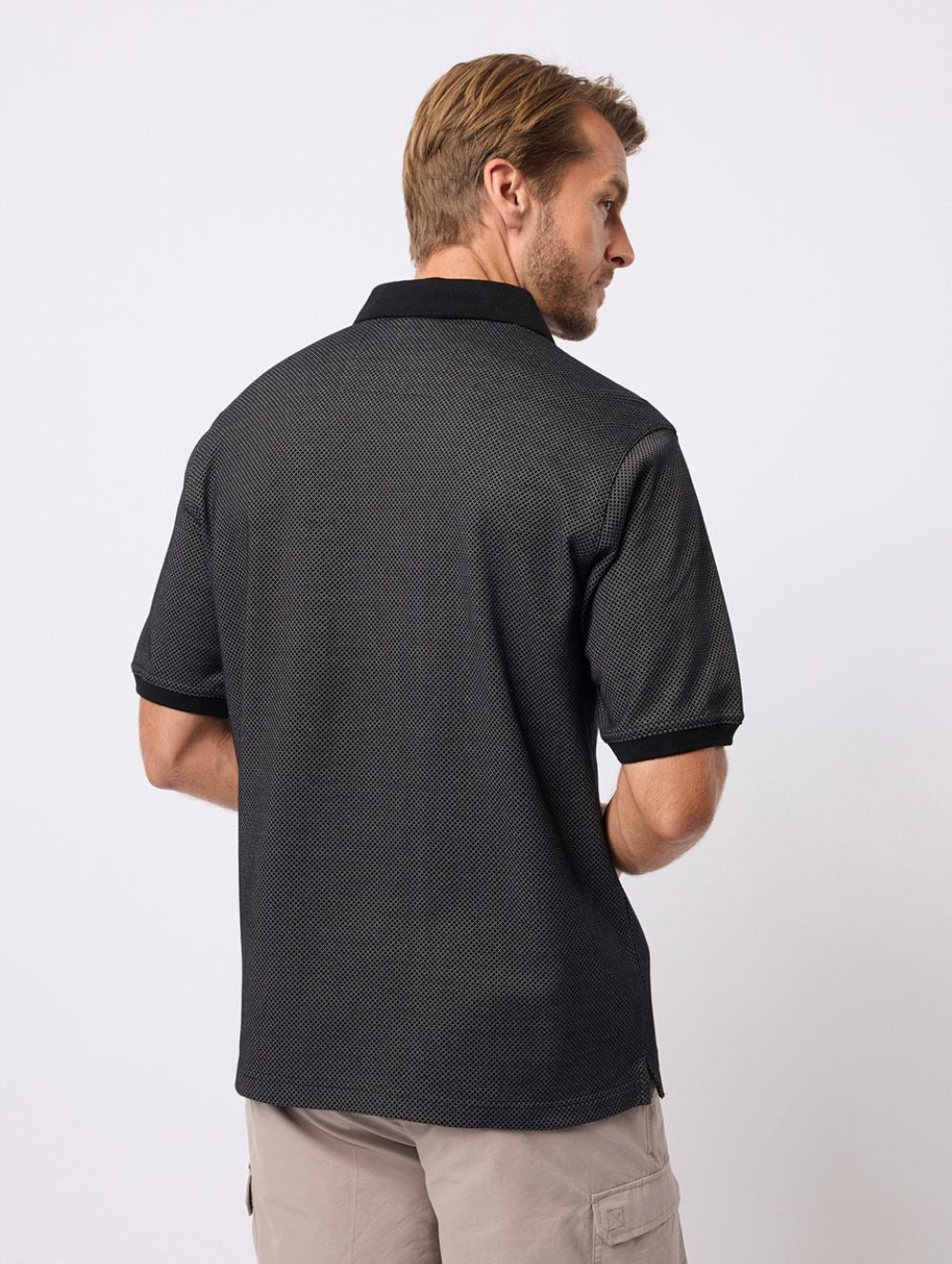 A man with light brown hair, facing away from the camera, wears the Breakaway Rafael Micro Prima Polo and light-colored cargo shorts against a plain white background.