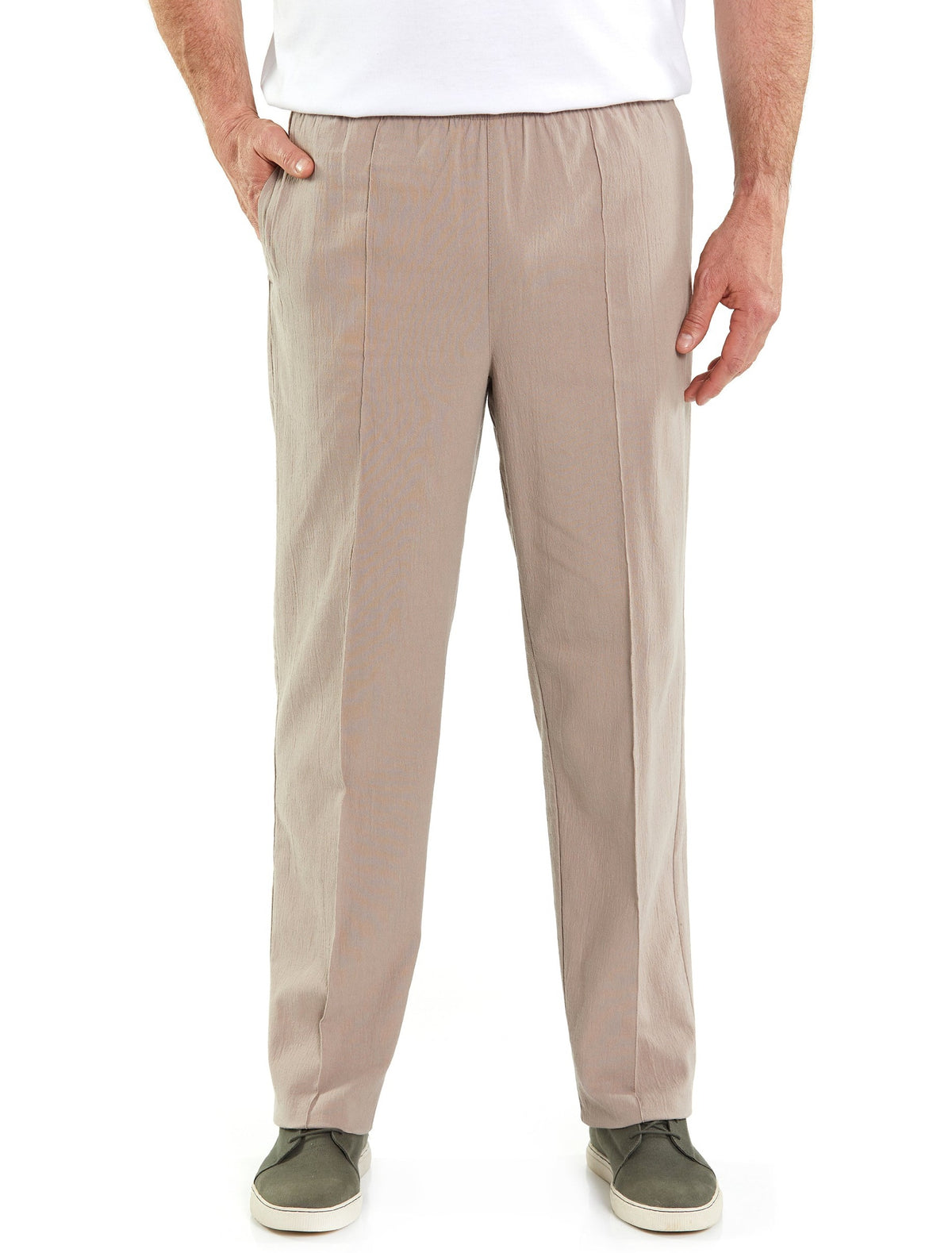 A person is standing against a white background wearing Breakaway Crinkle Pants in light beige, made of cotton with an elastic waist, and a tailored fit. They have their hands in both pockets. The individual is also wearing a white shirt and gray slip-on shoes with white soles.