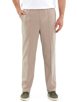 A person is standing against a white background wearing Breakaway Crinkle Pants in light beige, made of cotton with an elastic waist, and a tailored fit. They have their hands in both pockets. The individual is also wearing a white shirt and gray slip-on shoes with white soles.