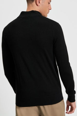 A man is seen from behind, wearing the Ben Sherman Merino Half Zip Knit in black with beige pants, standing against a plain light background.