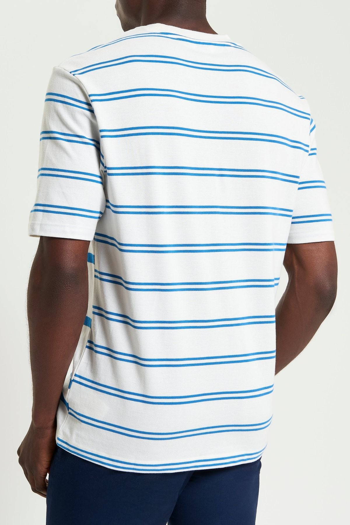 A person is seen from the back wearing the Ben Sherman Mixed Stripe Tee, featuring white fabric with blue horizontal stripes, and navy blue pants, standing against a plain light background.