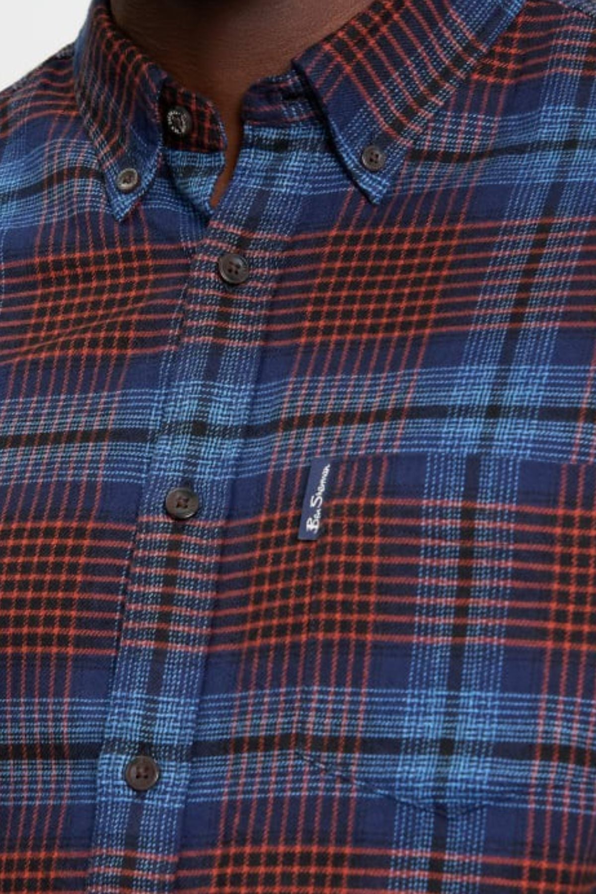 A close-up of a person wearing the Ben Sherman Ombre Check Shirt, featuring a blue and red plaid pattern, black buttons, and a small embroidered logo on the chest pocket.
