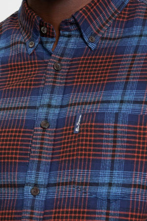A close-up of a person wearing the Ben Sherman Ombre Check Shirt, featuring a blue and red plaid pattern, black buttons, and a small embroidered logo on the chest pocket.