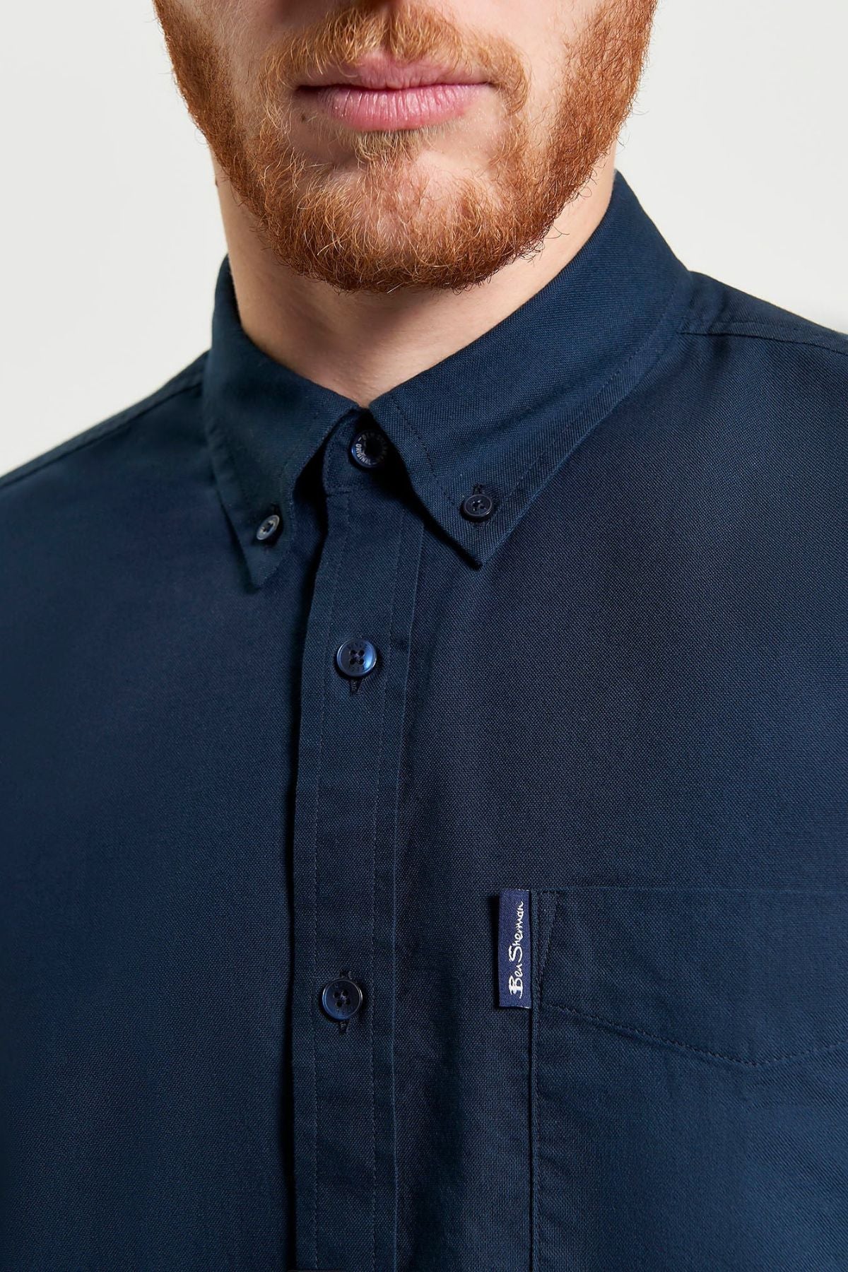 A man with a reddish beard wears a dark navy Ben Sherman Signature Oxford Short Sleeve Shirt with a collar and left chest pocket. It's made from organic cotton. The background is plain and light.