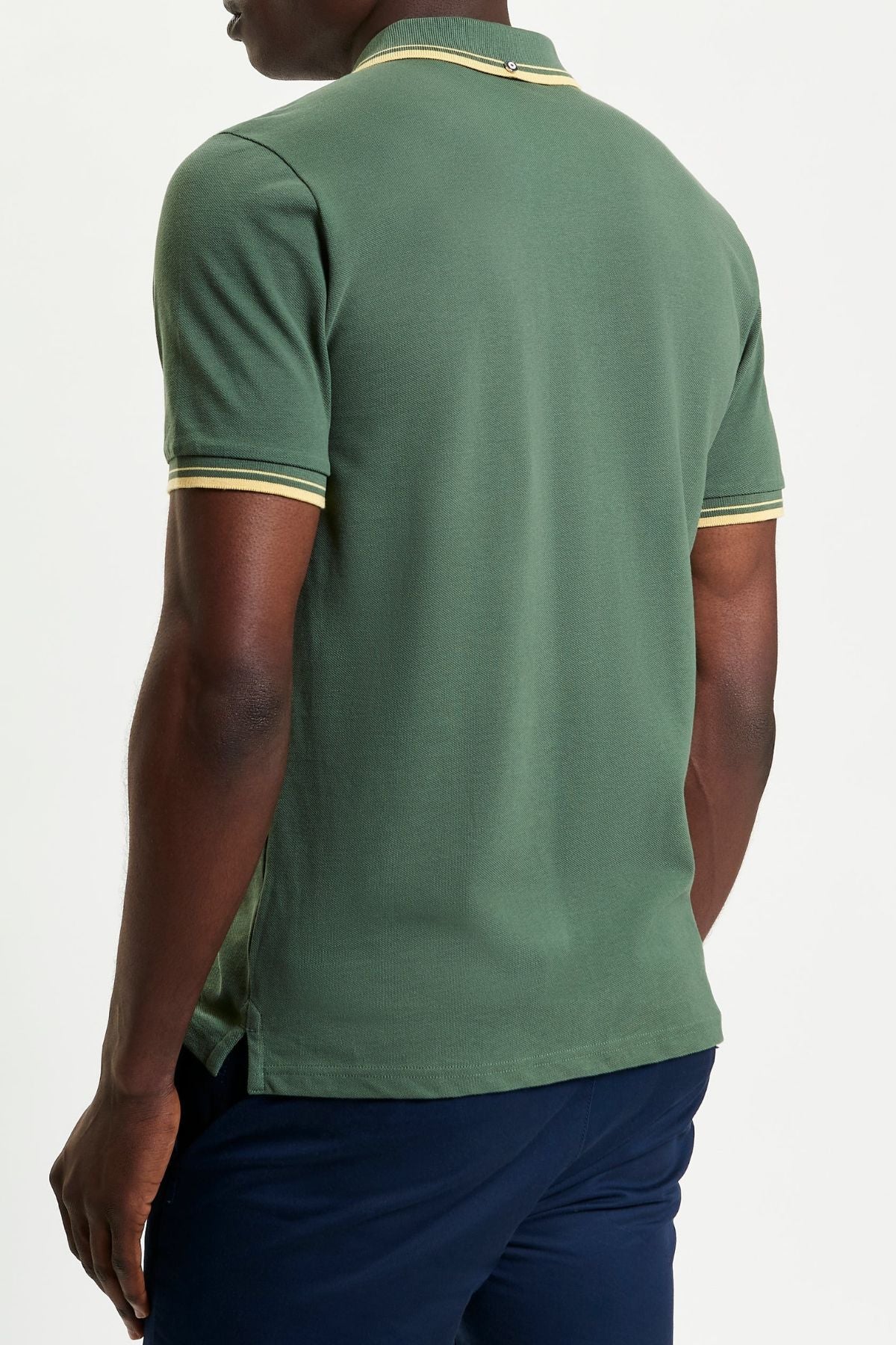 A person is shown from the back against a plain white background wearing a green Ben Sherman Signature Pique Polo with yellow-and-white trim on the sleeves and collar, paired with dark blue pants.