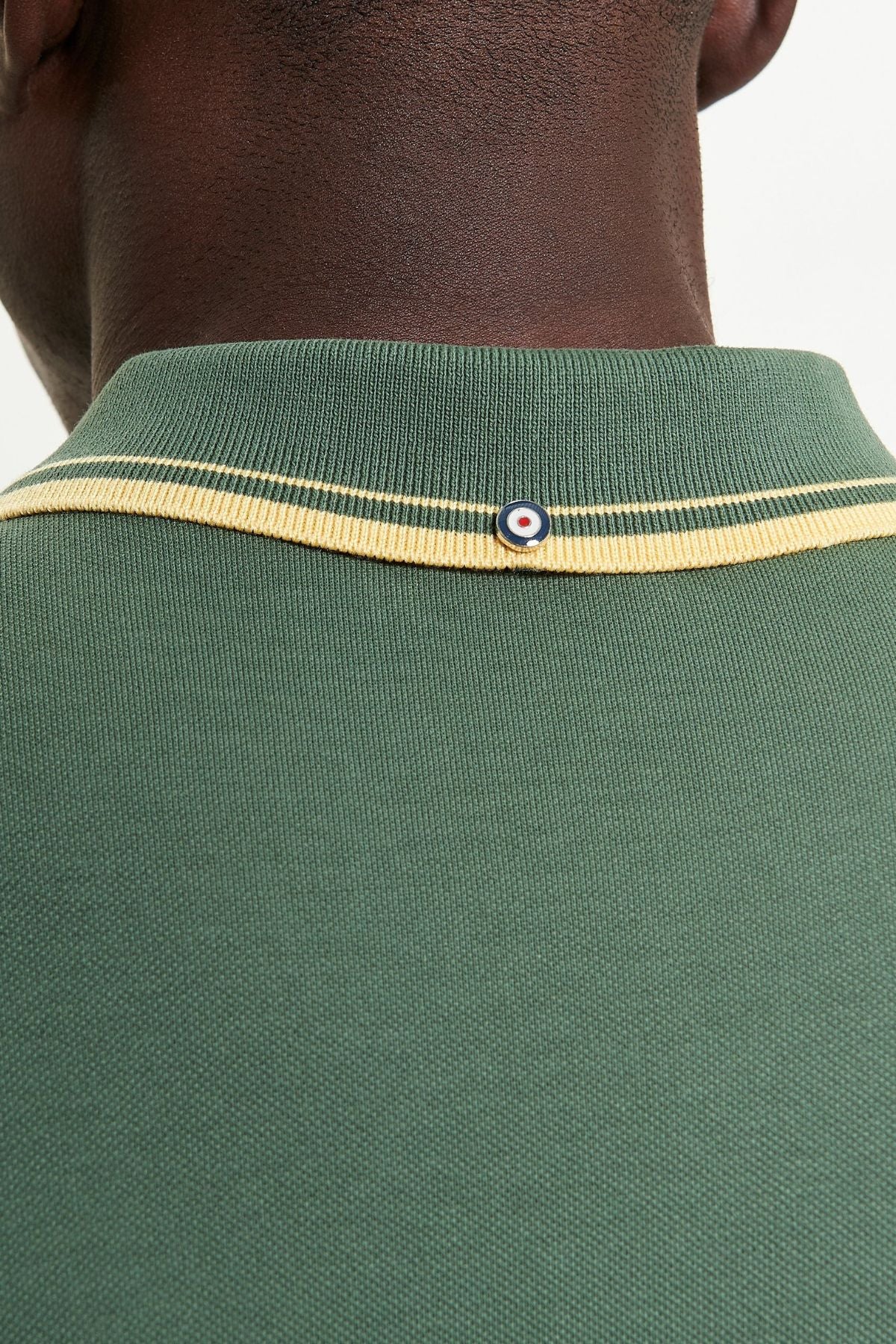 Close-up of the back of the Ben Sherman Signature Pique Polo in green, featuring a yellow-striped collar and a small round blue, white, and red emblem at the center, highlighting its classic style.