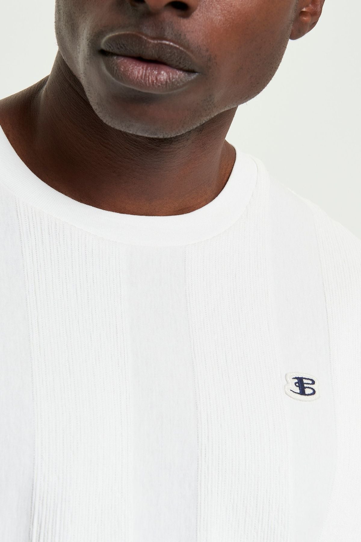 A close-up of a person wearing the Ben Sherman Textured Vertical Stripe Tee, featuring a white textured design and a small blue and white embroidered "TB" logo on the chest; only the lower half of their face is visible.