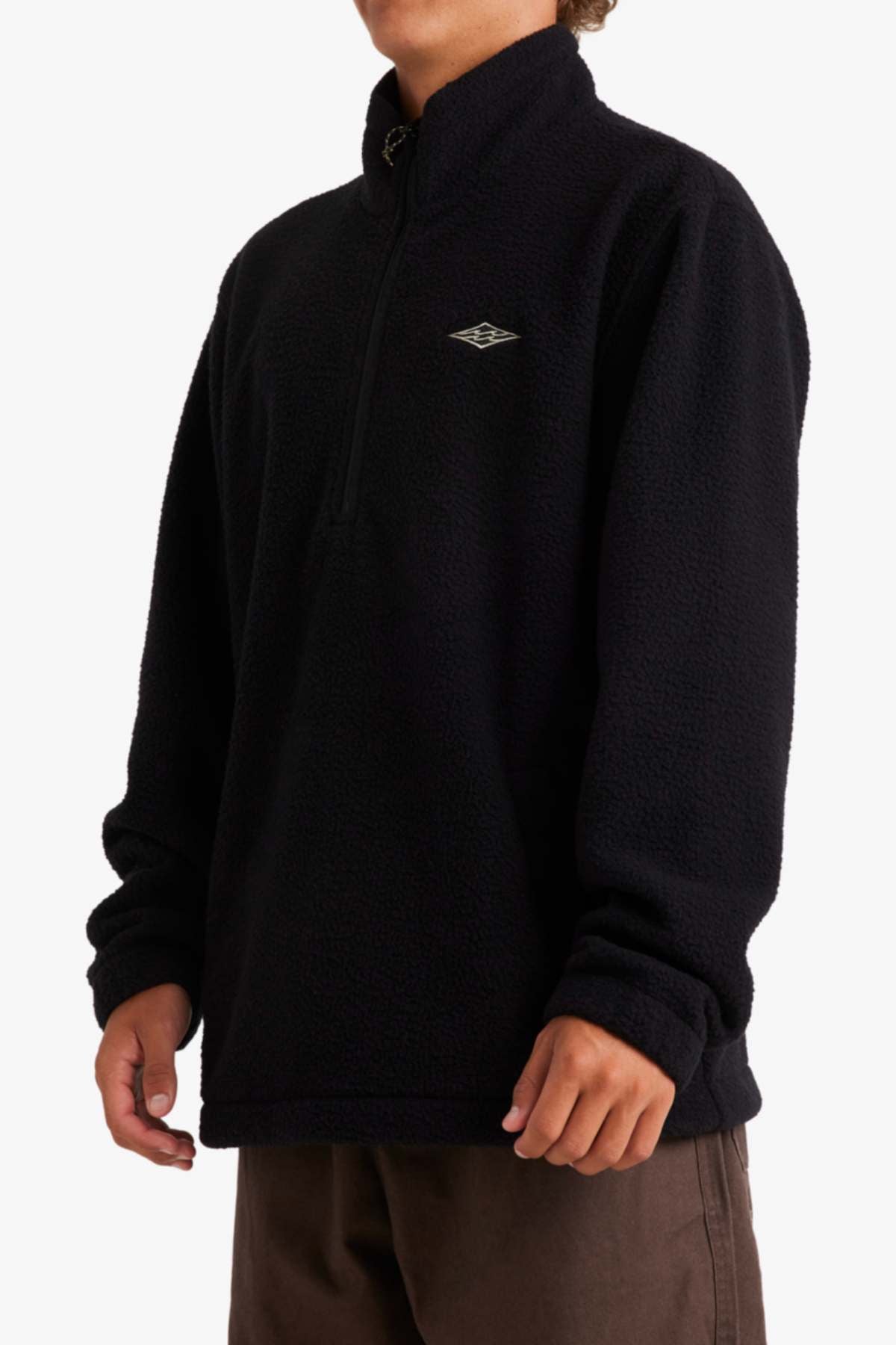 A person in a Billabong A/Div Boundary Mock Neck Sweatshirt, made from recycled polyester with a small chest logo and quarter-zip design, stands wearing brown pants against a plain white background.