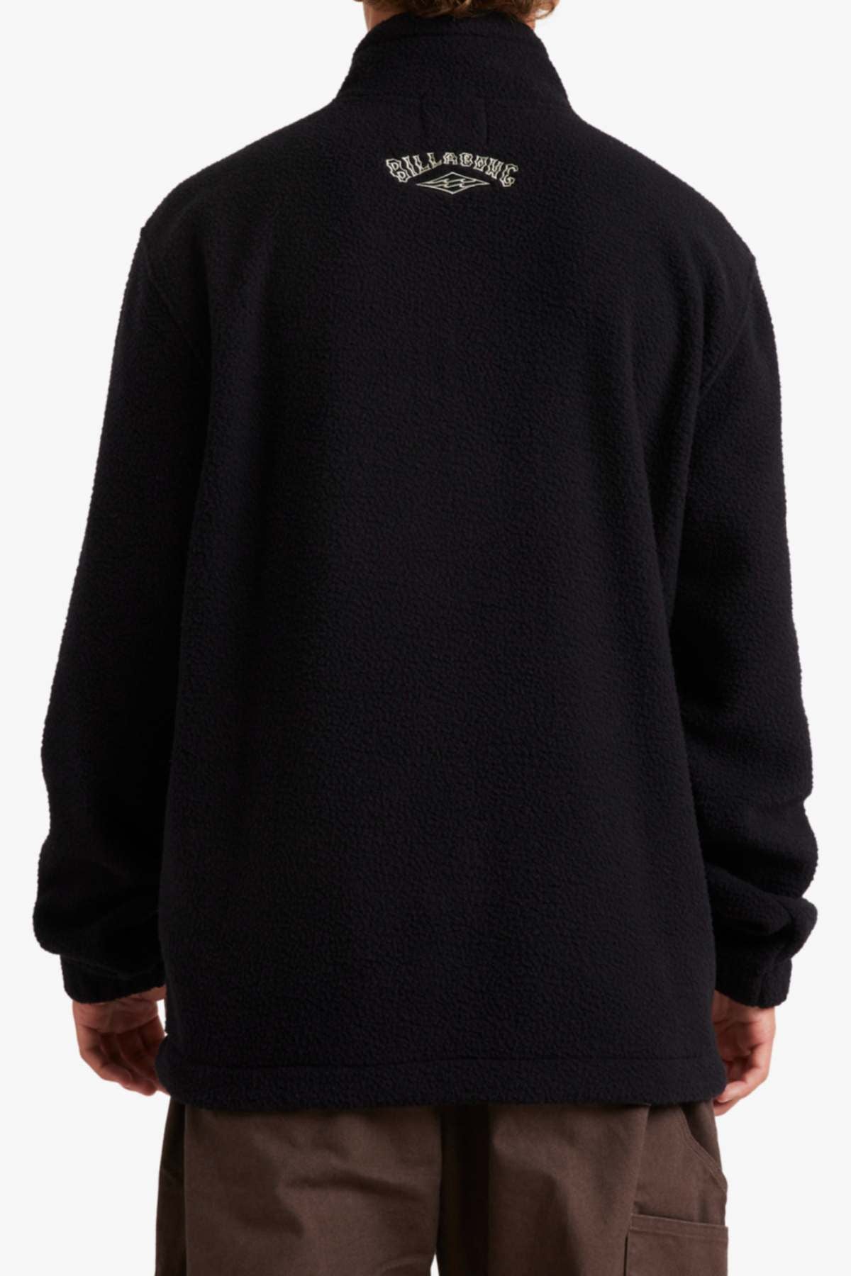 Wearing a Billabong A/Div Boundary Mock Neck Sweatshirt made from recycled polyester, the person, facing away, displays the logo on the upper back while the lower part partially covers their brown pants.