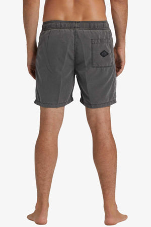 A person is seen from the rear wearing Billabong All Day Overdye Layback Short in dark gray. The shorts have an elastic waistband, a logo on the back pocket, and are made from eco-conscious fabric, with focus on the lower back and legs against a plain white background.