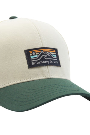 The Billabong Walled A/DIV Trucker hat, in beige and green, flaunts a logo patch with stylized mountains and sun, plus the "Billabong A/Div" text. Made from recycled polyester, it features a snapback for adjustable fitting.