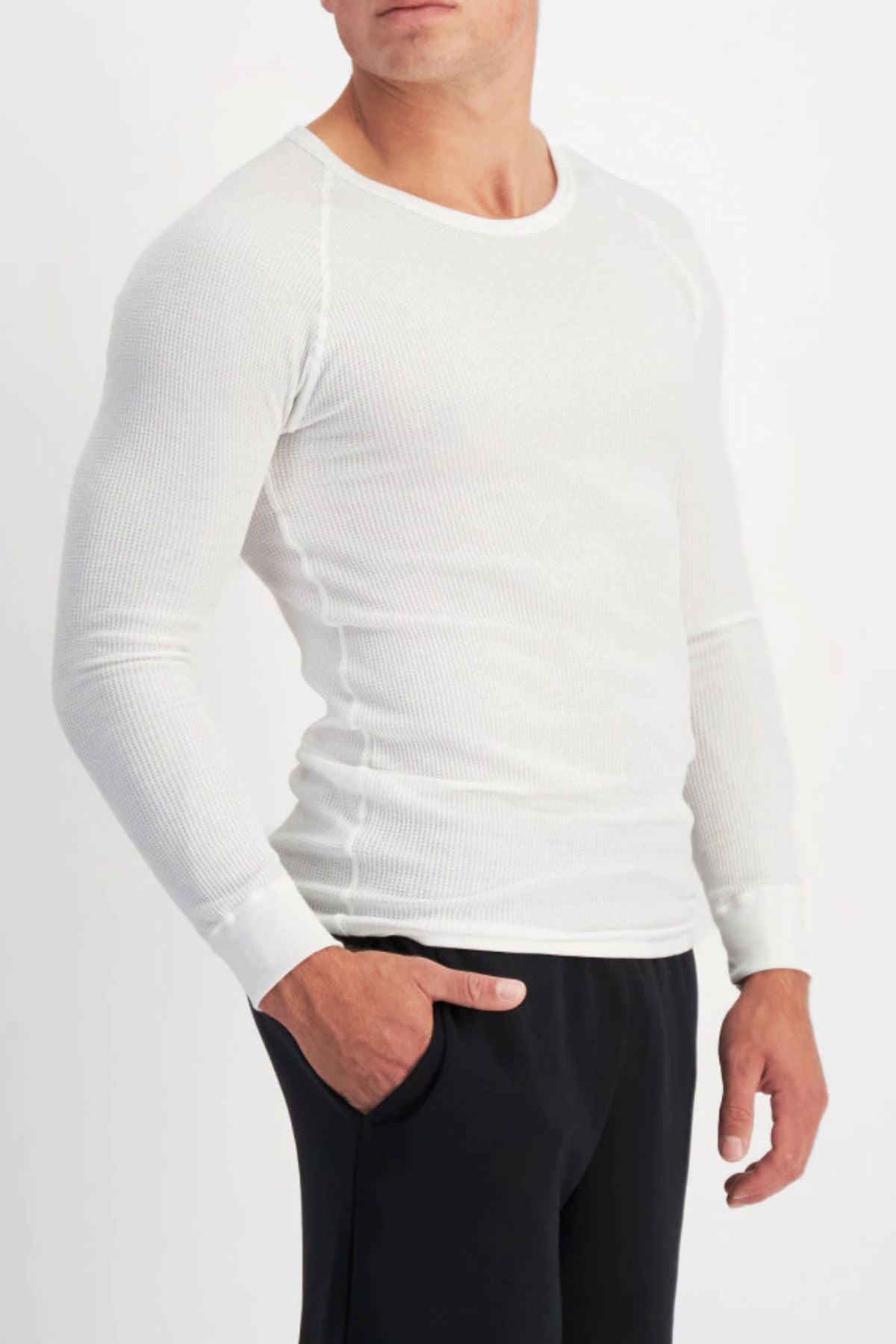 A man wearing a fitted Bonds Aircel Long Sleeve Tee and black pants stands with one hand in his pocket against a plain white background.