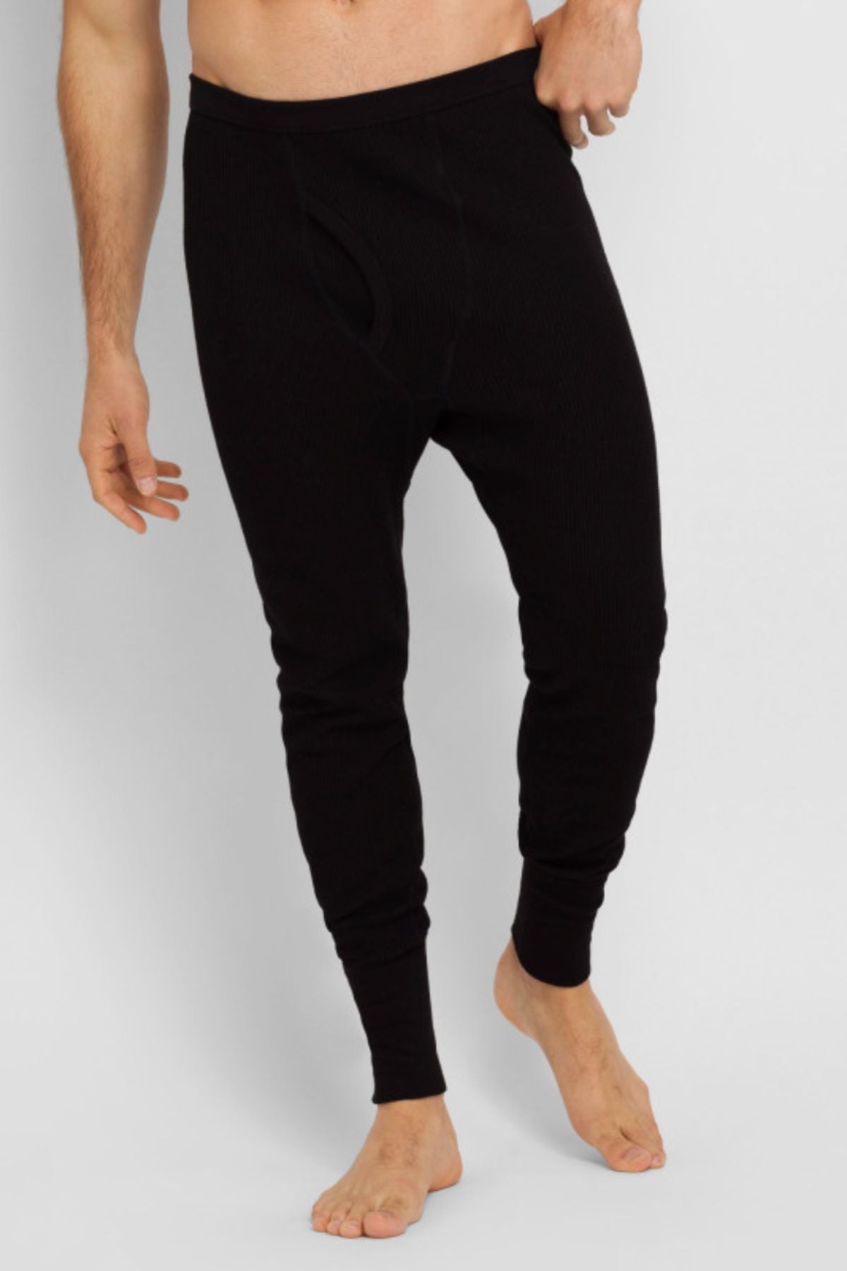 A man is wearing Bonds Aircel Thermal Long Johns made from stretchy fabric. He stands barefoot against a plain light background, one hand on his waistband and the other by his side.