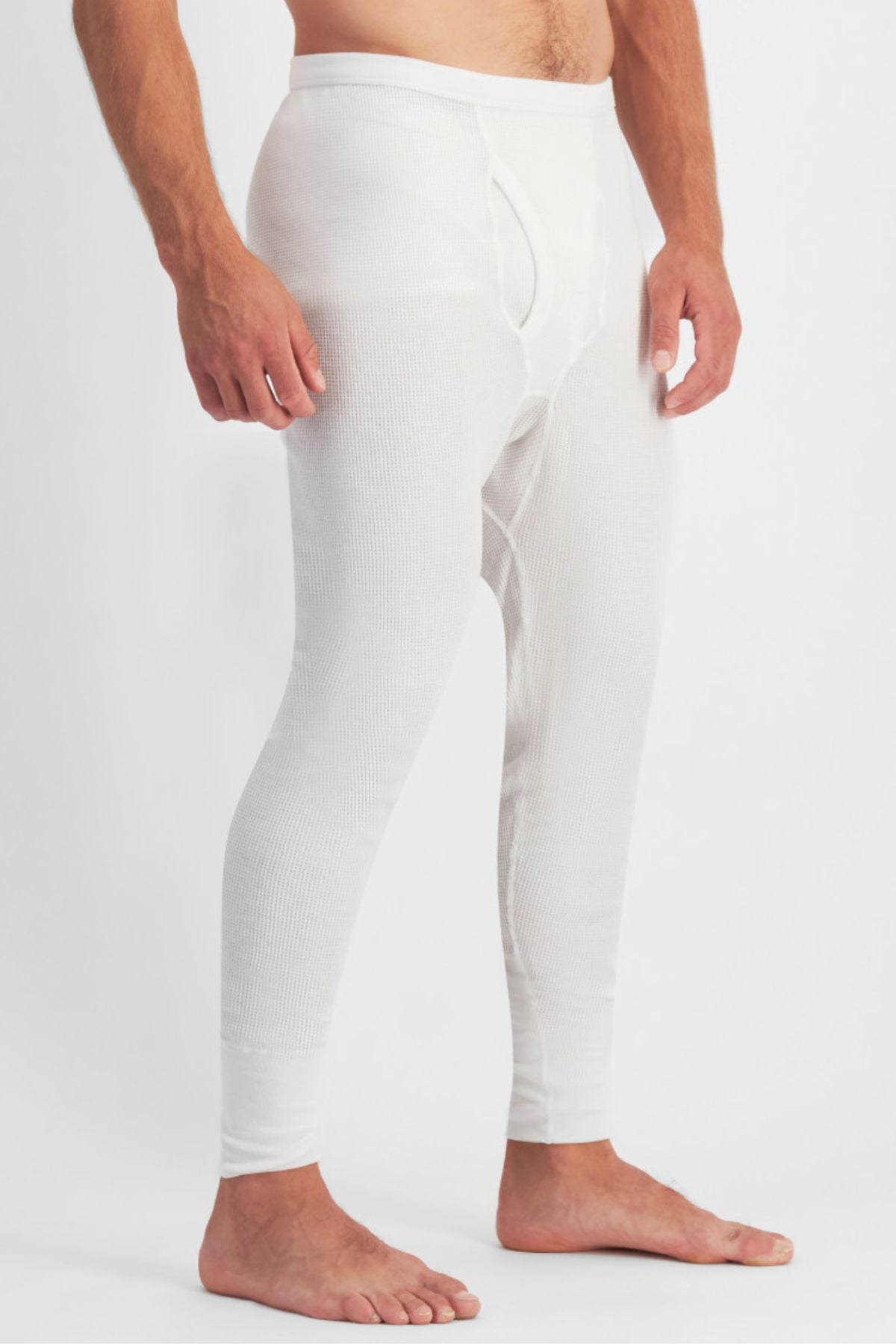 A man stands barefoot wearing Bonds Aircel Thermal Long Johns, shown from the shoulders down in side view, featuring a ribbed elastic waistband, visible front fly, and a comfortable ribbed texture.