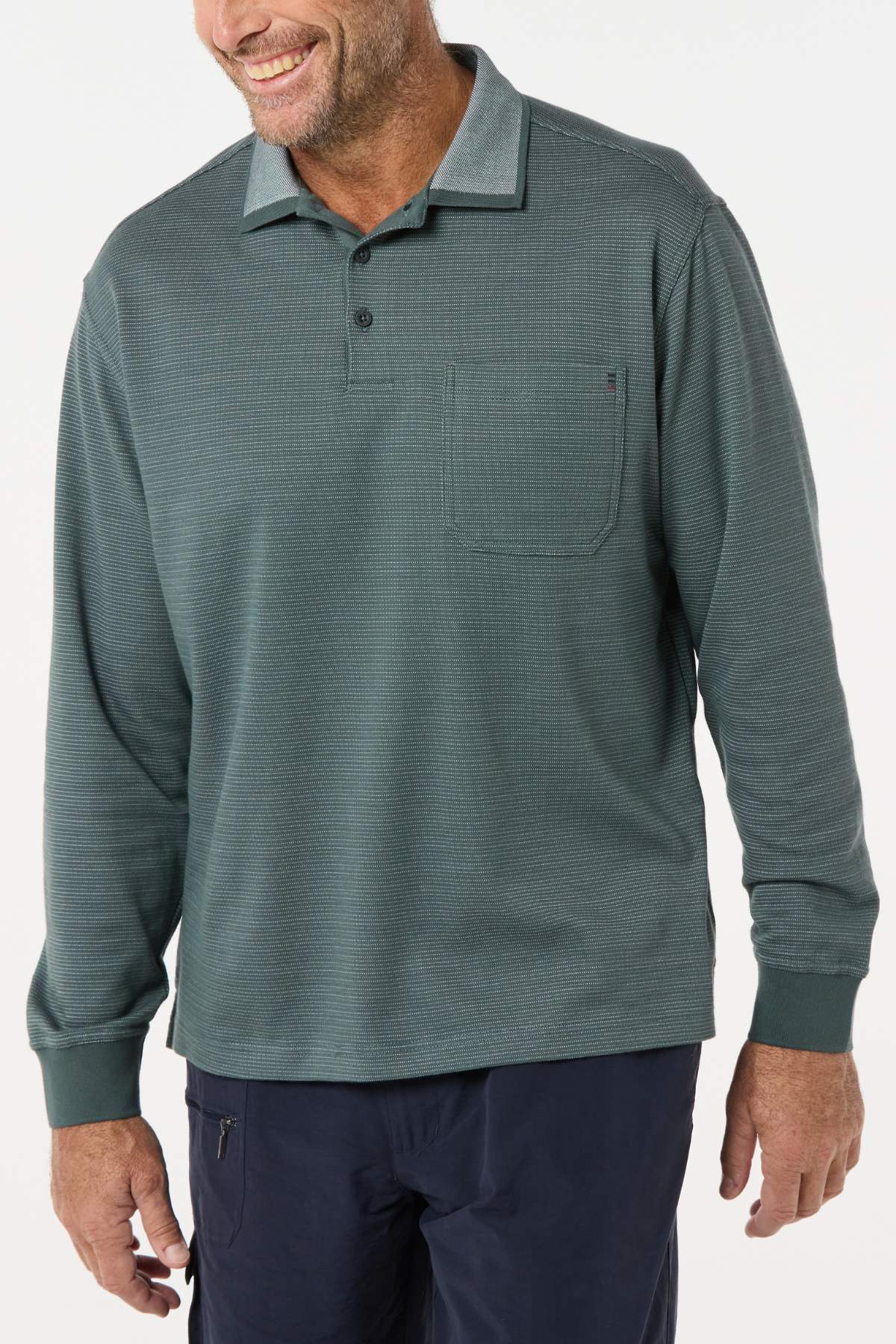 A man wearing a Breakaway Avantee Micro Prima Polo—a long-sleeve, teal-green collared shirt with rib knit cuffs and chest pocket—paired with dark pants, smiles against a white background for a timeless modern look.