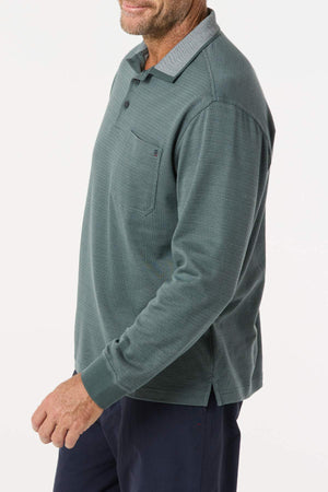 A man, face partially out of frame, stands against a white background wearing the Breakaway Avantee Micro Prima Polo in green with a chest pocket and rib knit cuffs, paired with navy pants.