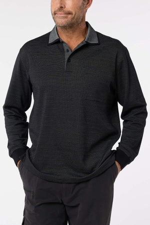 A man stands against a plain light background, hands in his pockets, wearing the Breakaway Avantee Micro Prima Polo—a long-sleeve style with a collar, chest pocket, and rib knit cuff—making it a truly versatile wardrobe staple.