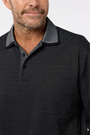 A man with a short beard wears the Breakaway Avantee Micro Prima Polo—dark, textured, featuring buttons, a pocket, and rib knit cuff—seen chest up against a plain light background. This versatile piece enhances any wardrobe.